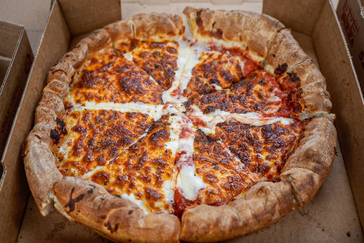 A pepperoni pizza with a thick, stuffed crust in a cardboard delivery box, cut into slices
